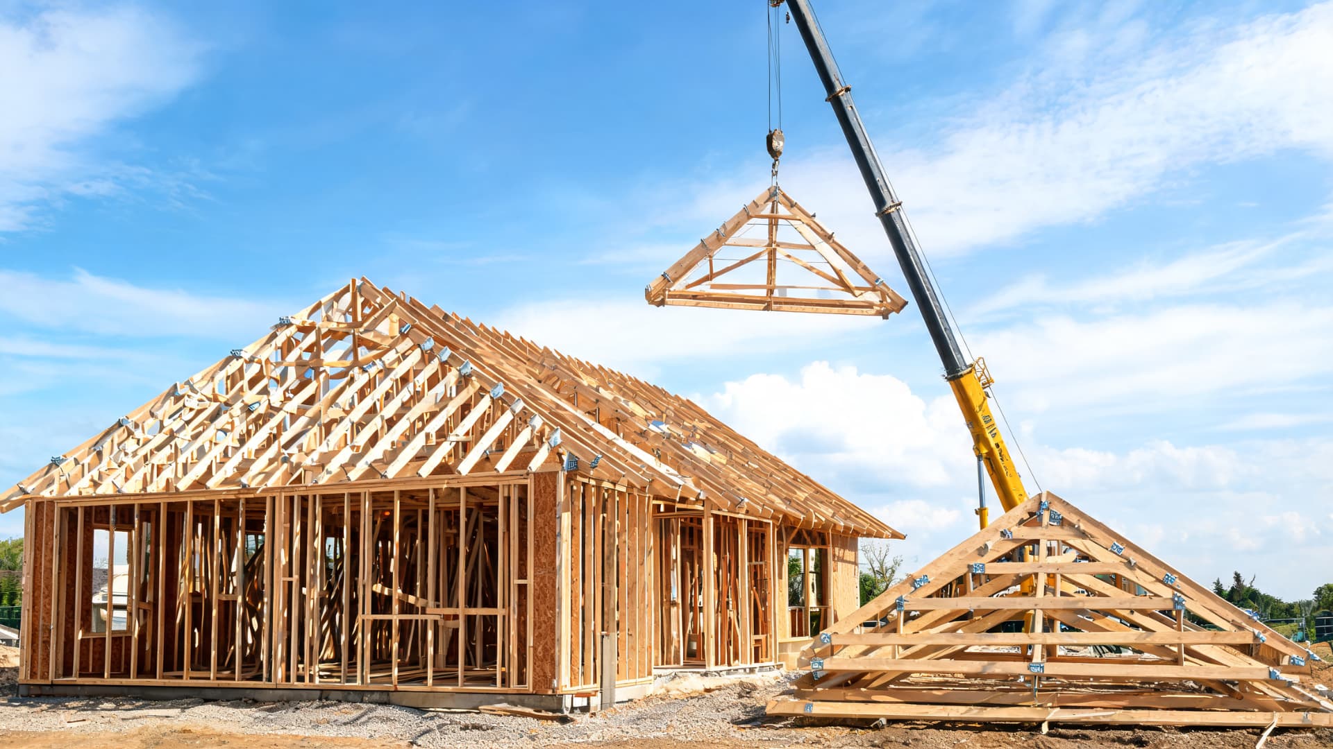 a crane lifts wooden roof trusses onto a new home frame during residential construction under a clear sky