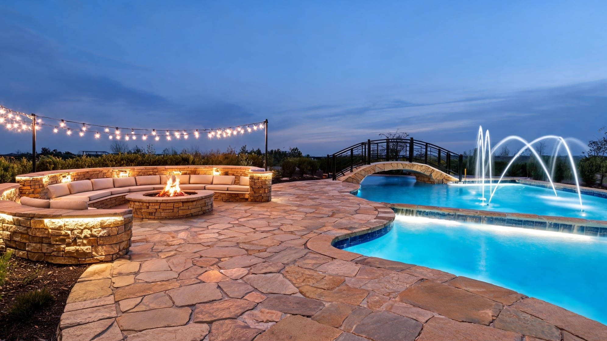 rock around pool ideas with flagstone patio fire pit seating bridge water fountains and warm evening lights