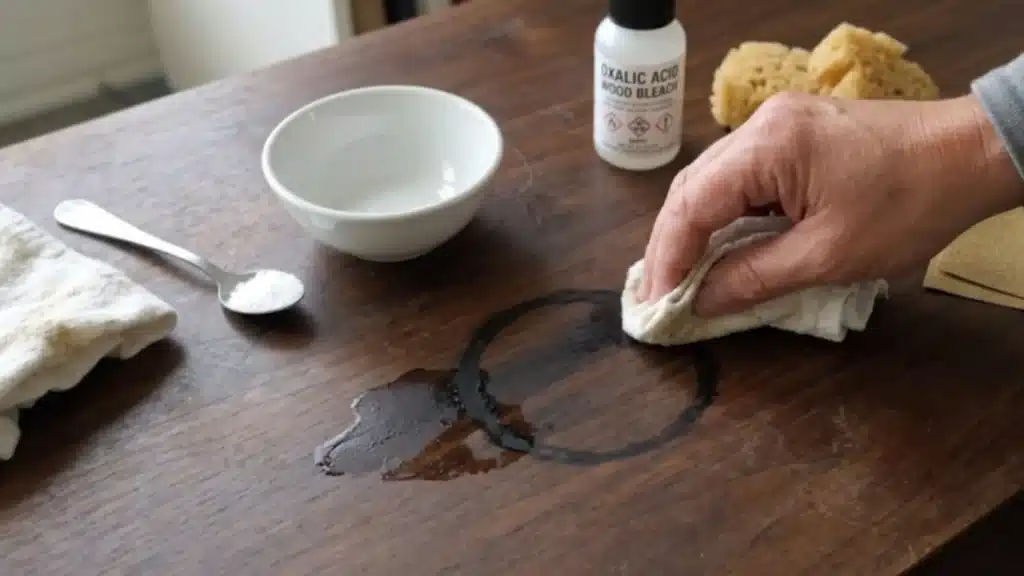 hand applies a cleaning agent to remove a deep black ring and liquid stain from a dark wooden table