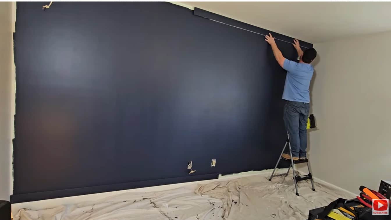 board and batten diy wall with dark paint finished and top edge board being installed near ceiling trim