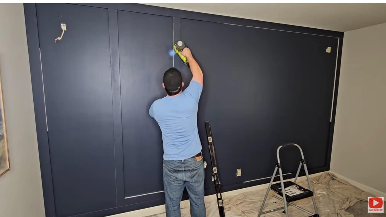 board and batten diy accent wall with vertical battens being nailed onto a dark painted wall during install