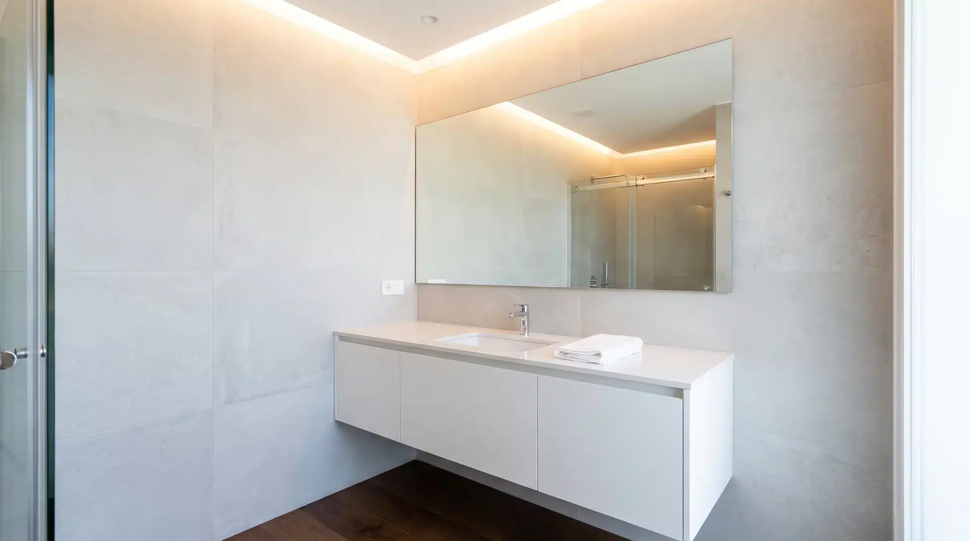 Modern guest bathroom with white floating vanity mounted to wall and large frameless mirror above.