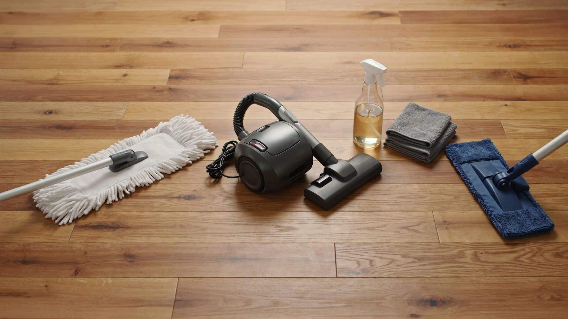 Hardwood floor cleaning tools including microfiber mop, vacuum, cleaner, and cloths on wood flooring.