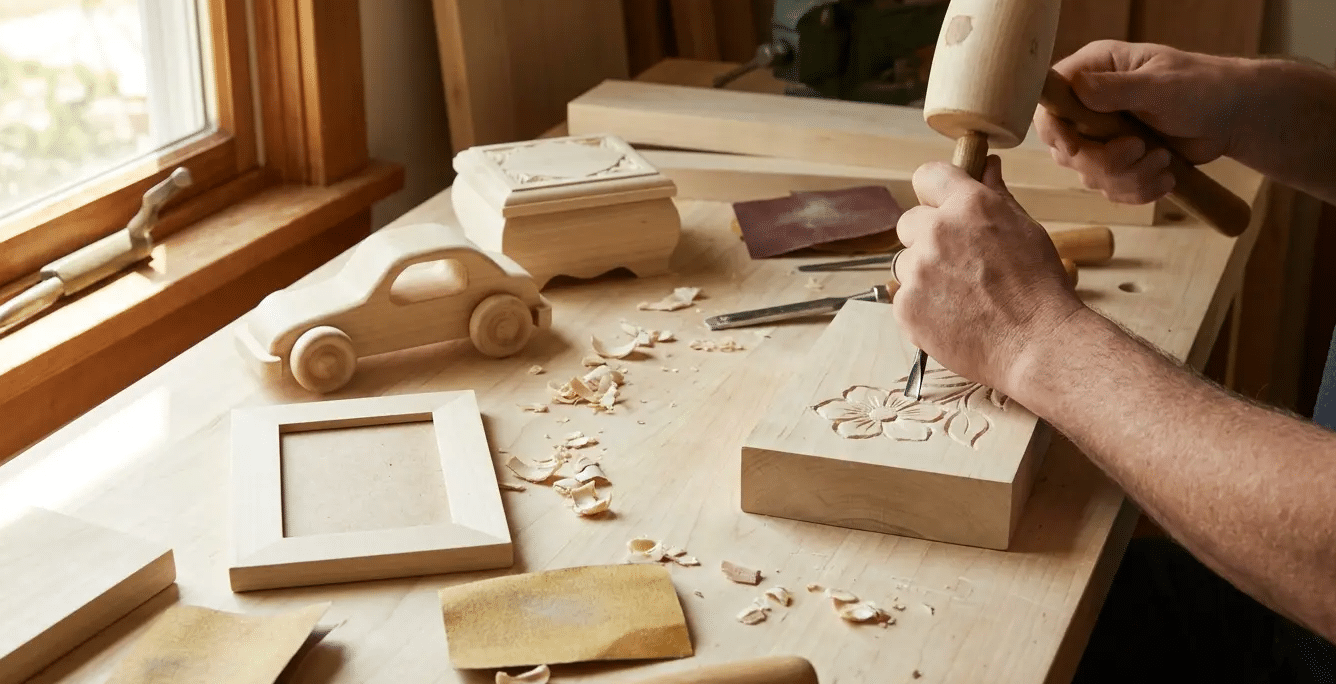 Person carving a wooden block with hand tools on a workbench during a small woodworking project.