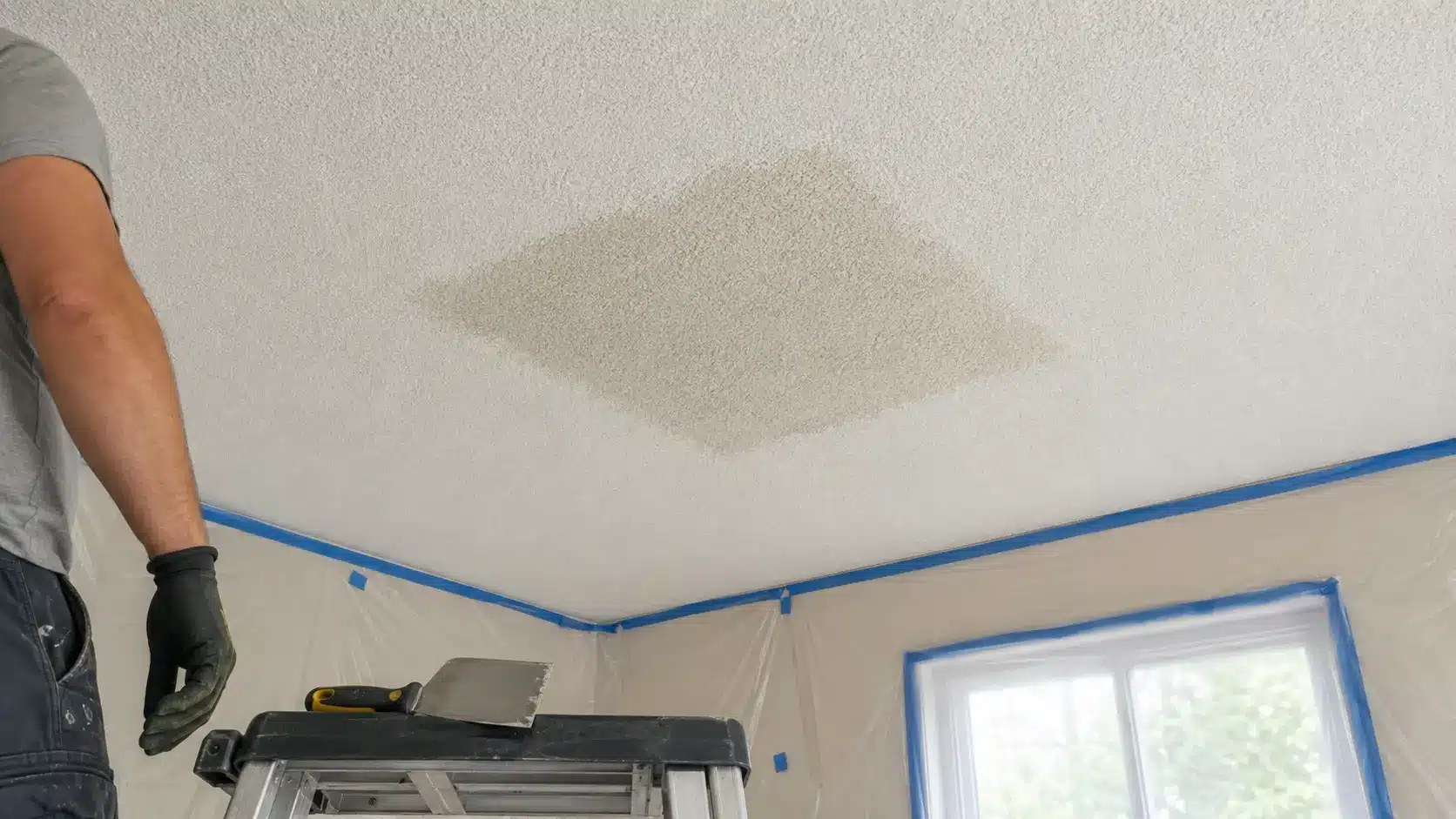 Worker letting a wet section of popcorn ceiling soften before scraping the texture away