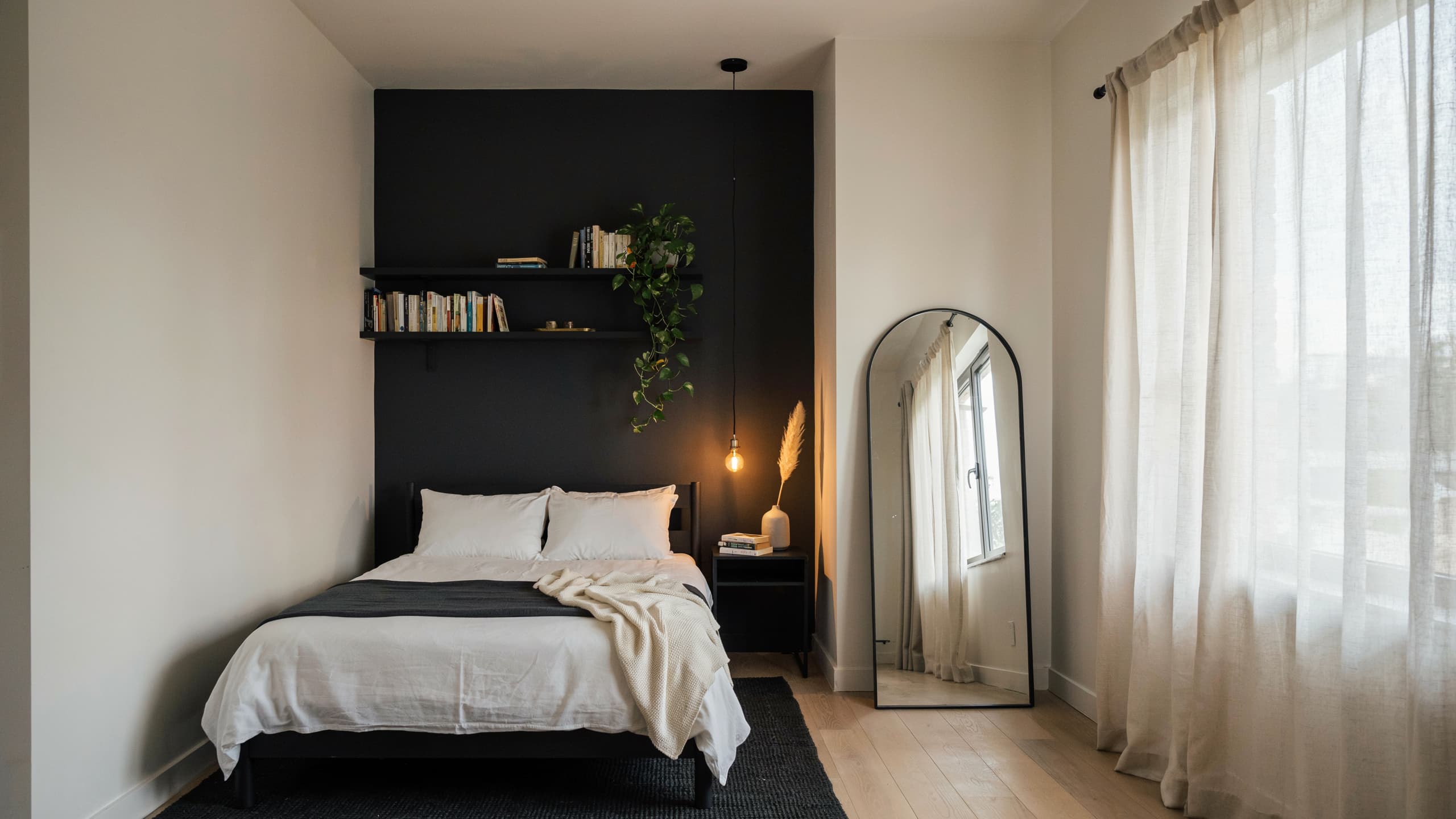 Small black bedroom with accent wall, mirror, and space-saving furniture