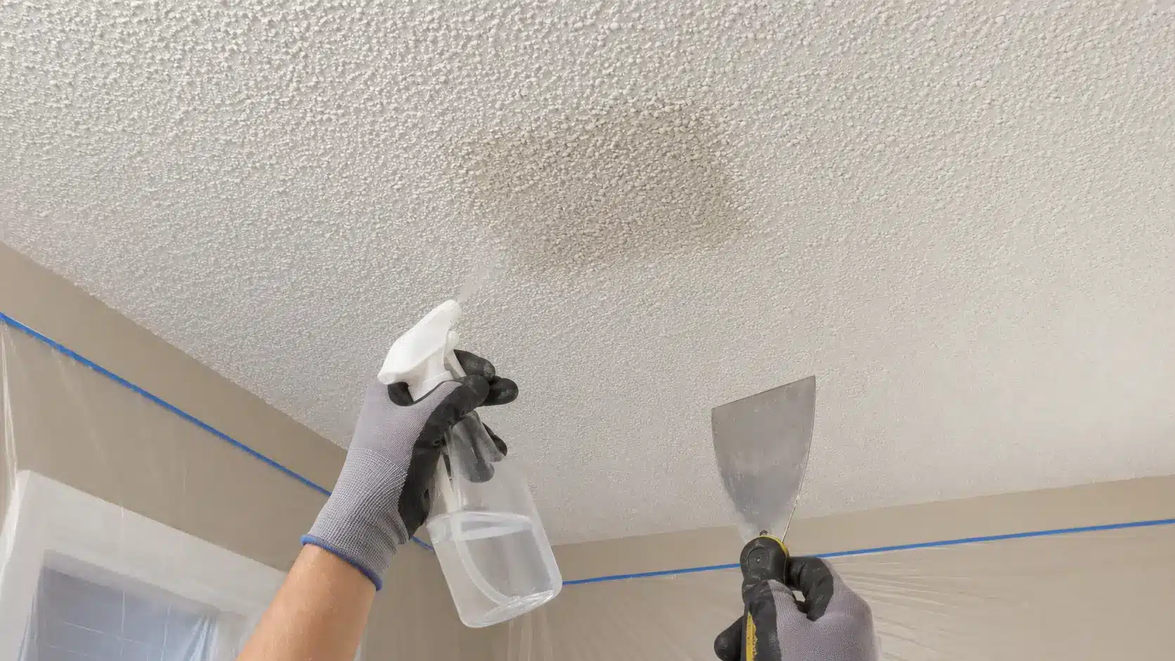 Testing a small area of a popcorn ceiling with water before scraping the texture.