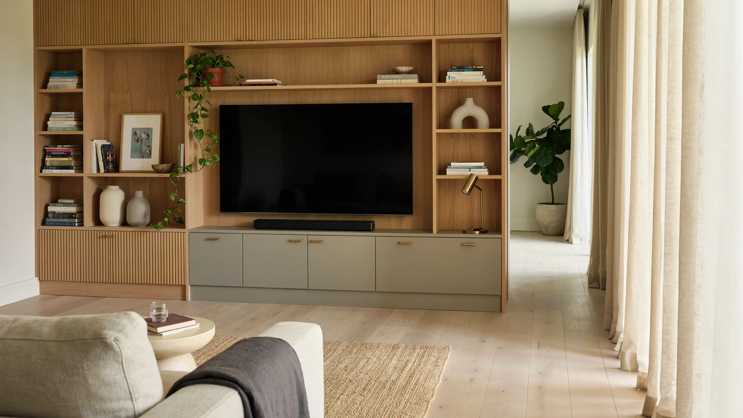 Built-in wooden entertainment armoire with TV, shelves, decor, and storage cabinets in a modern living room.